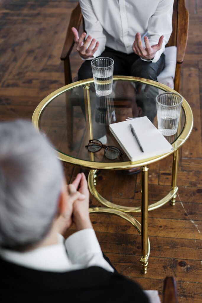 pexels-photo-4098369-4098369 Two adults discussing mental health in a counseling session across a glass table indoors.