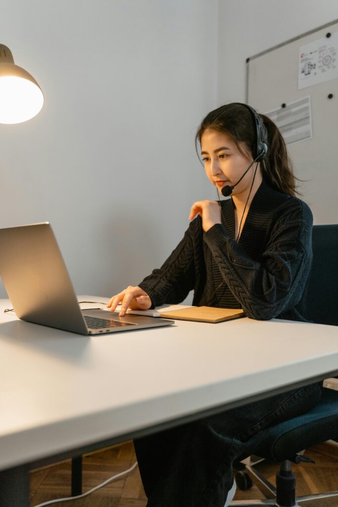 pexels-photo-7709289-7709289 Asian woman in headset working on a laptop. Ideal for customer support themes.